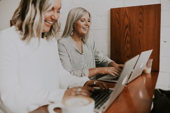 two women using laptops and smiling